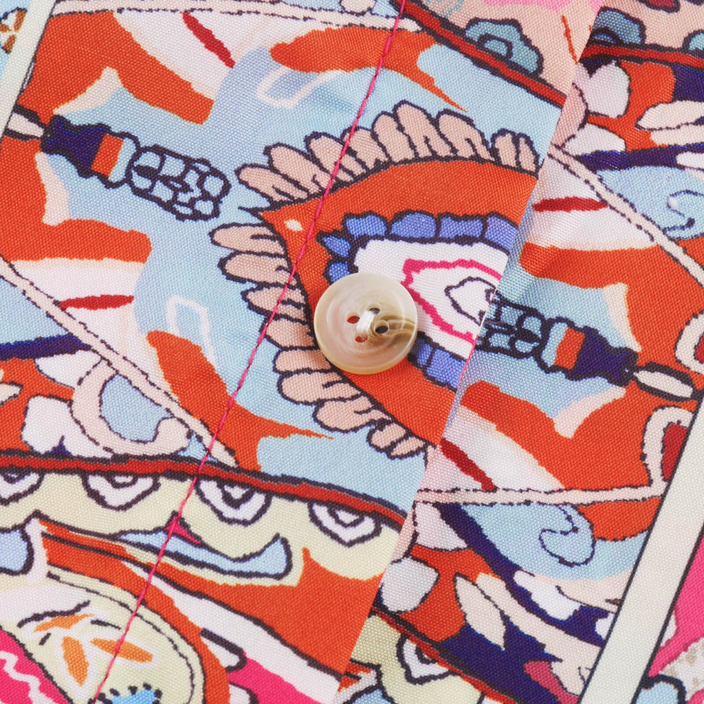 Primer plano del tejido: botón nacarado y pespunte rosa sobre estampado paisley