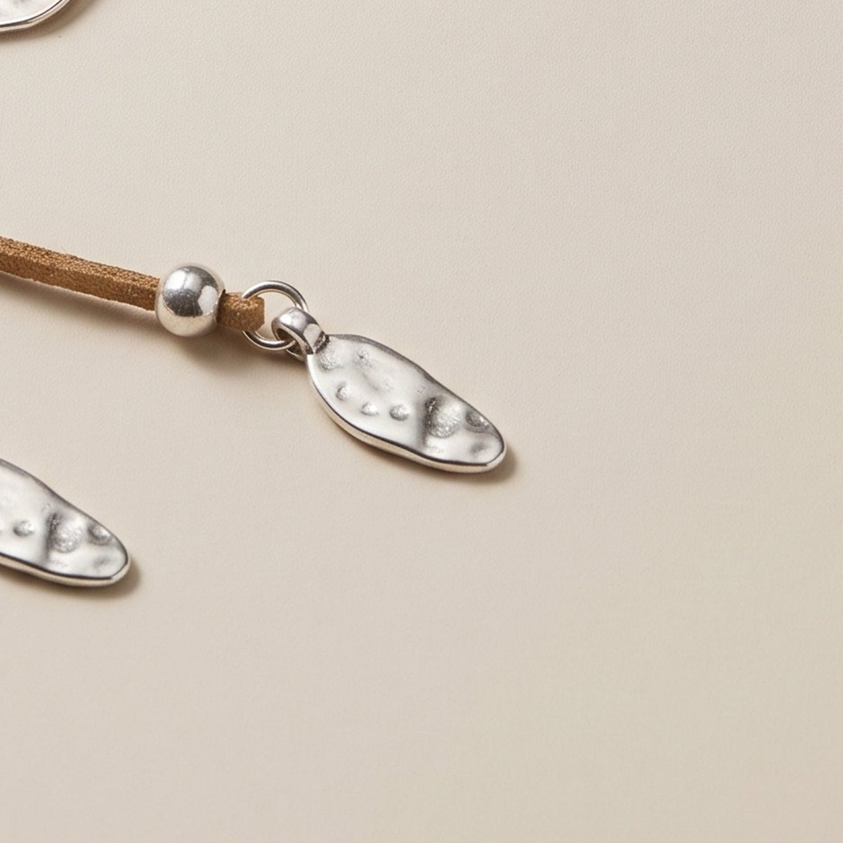 Close-up of the hammered oval charm on a suede strand