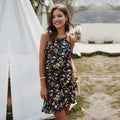 Lachend model draagt de marineblauwe boho jurk met bloemen en halterhals