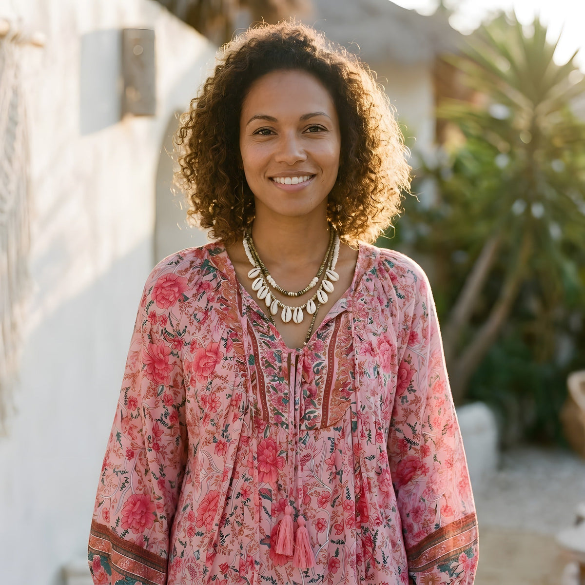 Smiling model wearing pink floral hippie blouse with laced pompom neckline