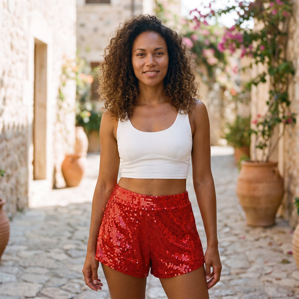 Lächelndes Model in roten Pailletten-Shorts auf gepflastertem Weg