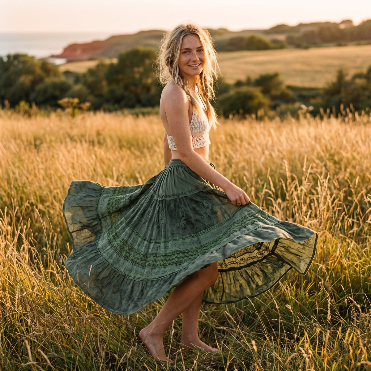 Smilende kvinde drejer rundt i lang skovgrøn boho blondenederdel på solrig eng