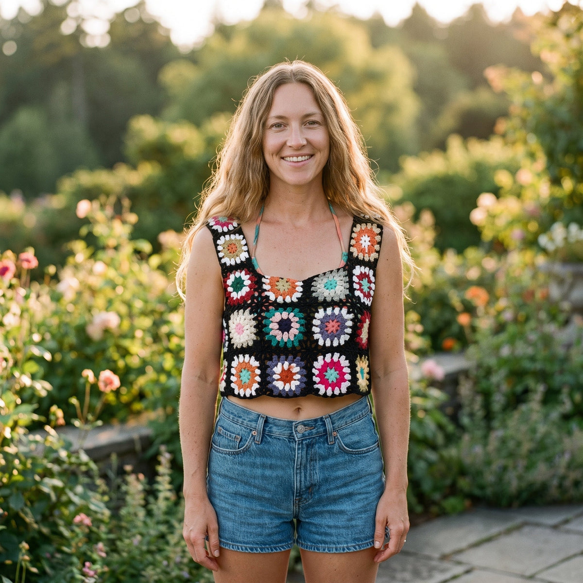 Black granny square crochet crop top worn by a smiling model in a garden
