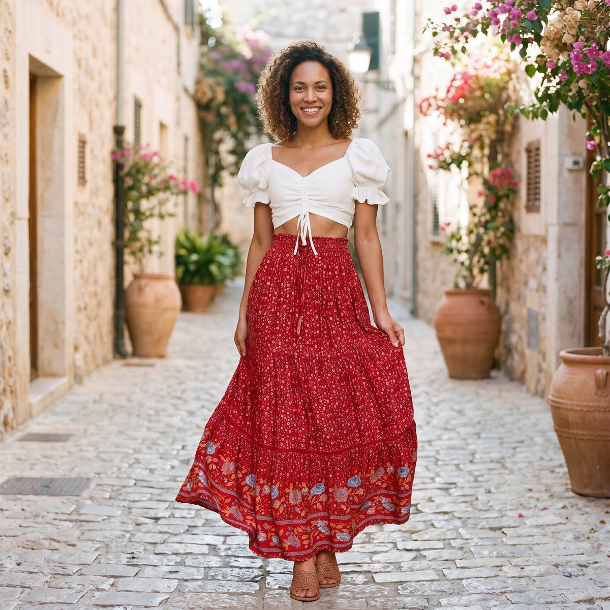 Smiling model wearing a long red floral hippie skirt in a sunny alley