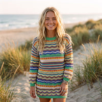 Lächelndes Model trägt das bunte Strick-Pulloverkleid an einem Strand
